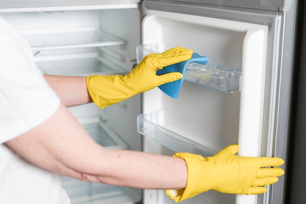 Foto mujer con guantes de goma limpiando nevera