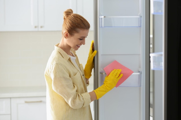 Mujer con guantes de goma limpiando el refrigerador vacío en casa