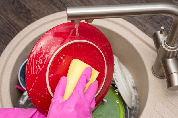 Foto la mujer con guantes de goma protectores rosados está lavando los platos en la cocina