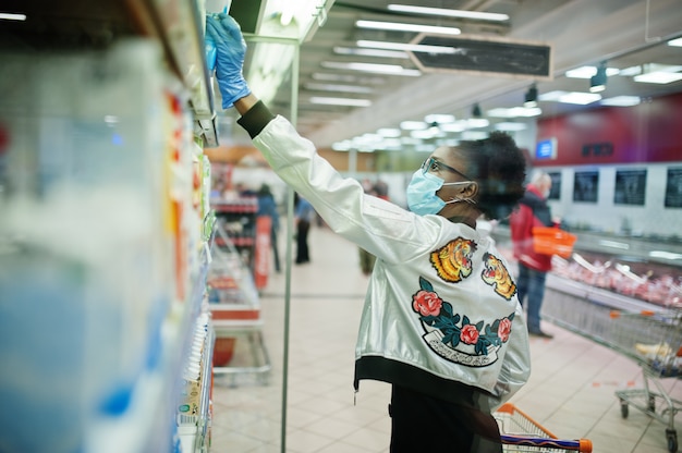 Mujer con guantes y máscara médica desechable de compras en el supermercado durante el brote de pandemia de coronavirus.