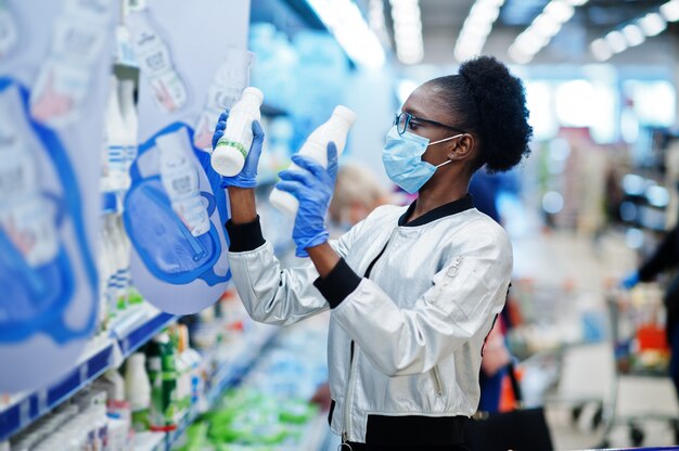 Mujer con guantes y máscara médica desechable de compras en el supermercado durante el brote de pandemia de coronavirus.