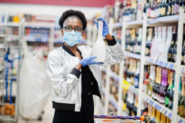 Mujer con guantes y máscara médica desechable de compras en el supermercado durante el brote de pandemia de coronavirus.