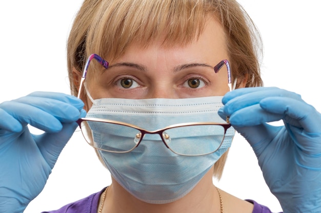 Una mujer con guantes y una mascarilla se está poniendo gafas como protección contra un virus en el aire