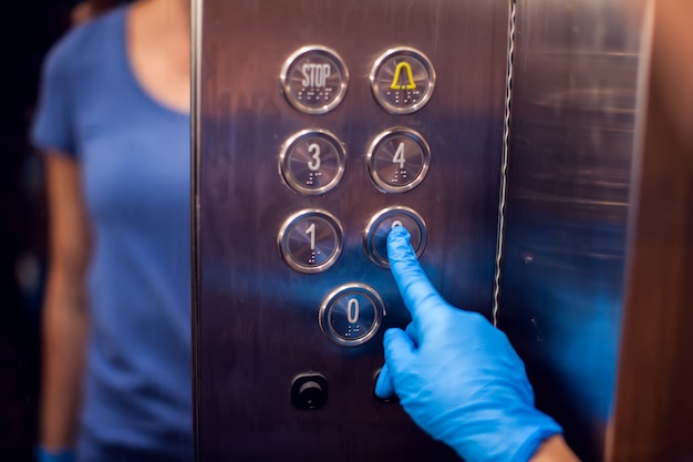 Foto mujer con guantes médicos presionando el botón en el elevador. de cerca. concepto de higiene y sanidad