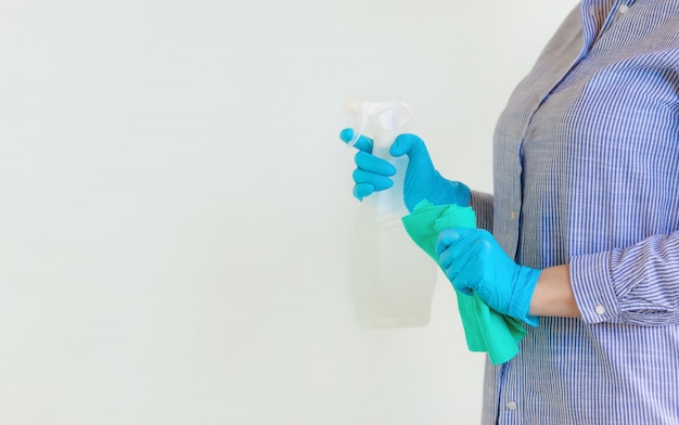 Mujer en guantes protectores limpiando el polvo con un spray y un plumero mientras limpiaba su casa.