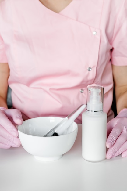 Mujer en guantes rosas con tazón de fuente blanco y cepillos cosméticos