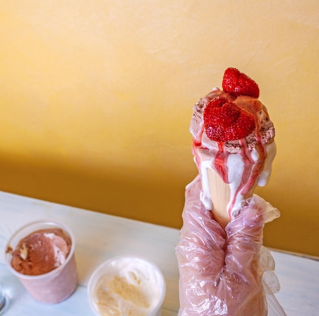 Una mujer con guantes sostiene un refrescante helado de chocolate y vainilla con fresas en un cono