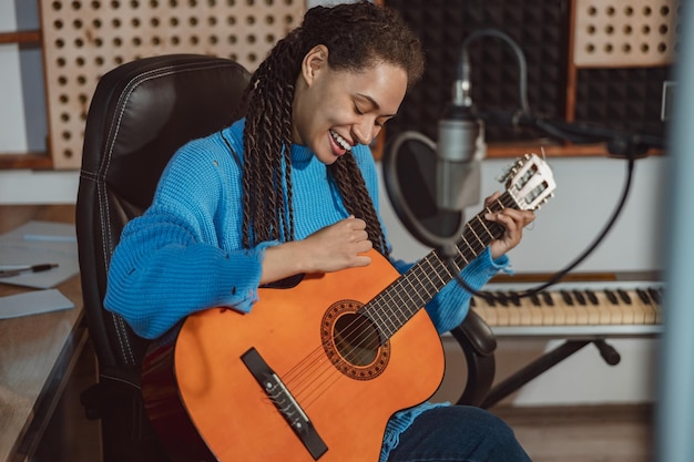 Mujer guapa africana músico compositor guitarrista toca la guitarra y ensaya una nueva canción en un estudio de grabación profesional