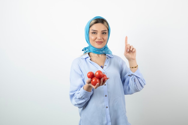 Mujer guapa en chal mostrando el número uno con la mano y sosteniendo tomates rojos