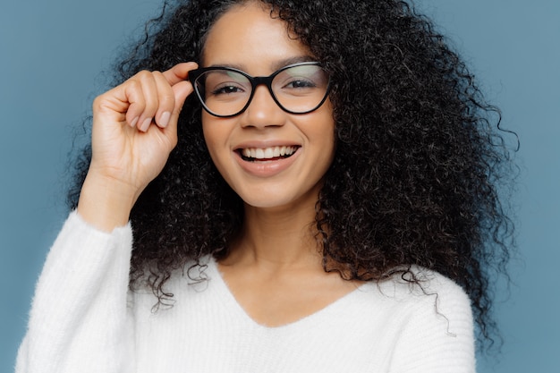 La mujer guapa usa lentes ópticos, sonríe ampliamente, muestra dientes blancos y perfectos