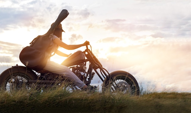 Mujer del guitarrista que monta una motocicleta en el camino del campo, fondo de la puesta del sol