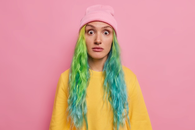 Foto la mujer se ha preguntado la expresión de la cara emocionada mira fijamente emboscada a la cámara lleva sombrero puente amarillo aislado en rosa