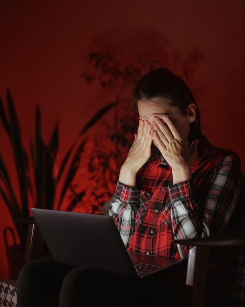 Una mujer en una habitación oscura está trabajando en una computadora portátil o viendo una película y jugando videojuegos como freelance