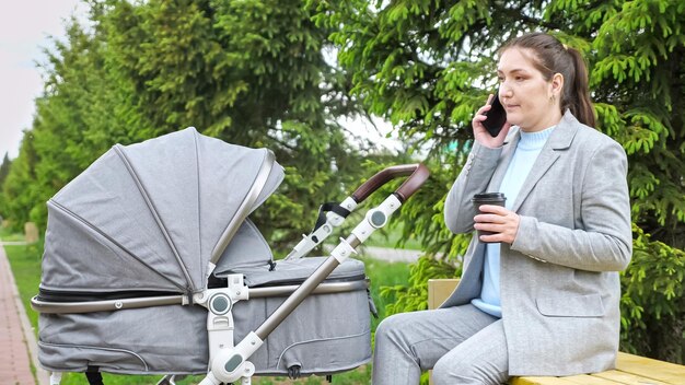 Mujer habla por teléfono sentada en un banco cerca de un cochecito en el parque