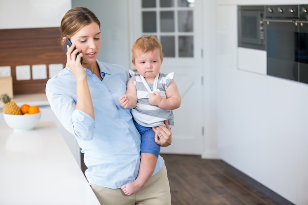 Mujer hablando por teléfono móvil mientras llevaba hija