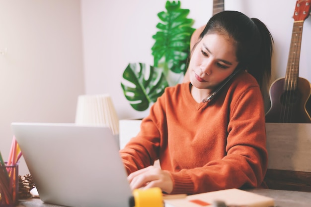 Mujer hablando por teléfono móvil mientras usa una computadora portátil en casa