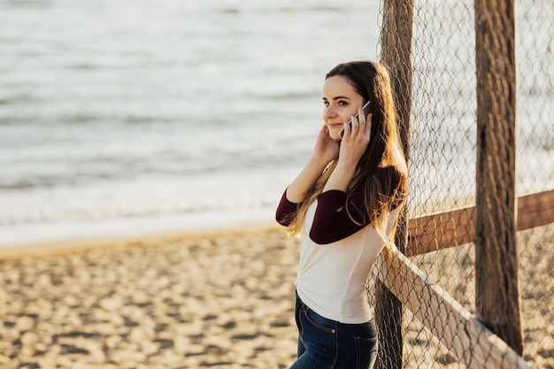 Mujer hablando por teléfono móvil en una playa con fondo de mar