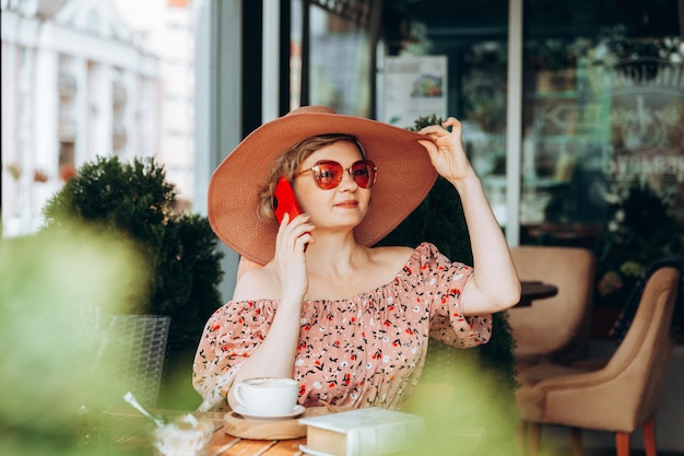 Una mujer hablando por teléfono Una mujer con un teléfono móvil está sentada en un café Una mujer con un vestido y un sombrero en un café