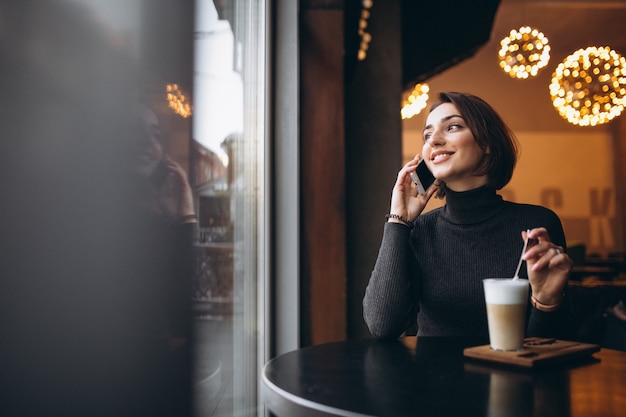 Mujer hablando por teléfono y tomando café en una cafetería