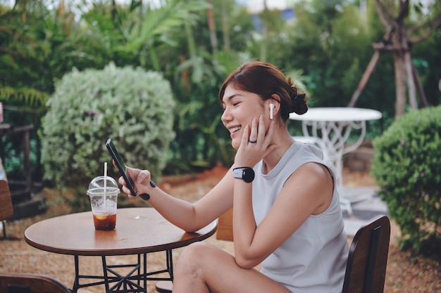 Mujer hablando en video chat a través de móvil digital y airpod blanco inalámbrico mientras está sentado