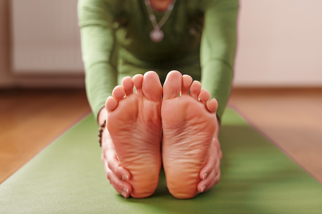 Una mujer hace asanas de yoga sobre una alfombra verde en la sala de estar