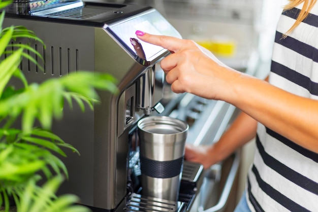 Una mujer hace café con sabor fresco con una máquina de café moderna en su cocina