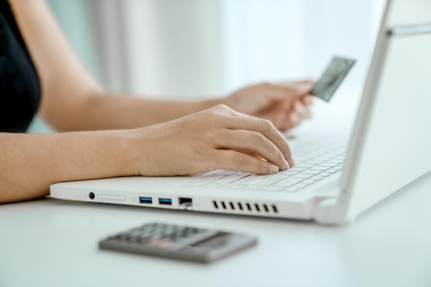 La mujer hace compras en línea sentada frente a la computadora portátil con la tarjeta bancaria en el primer plano de la mano