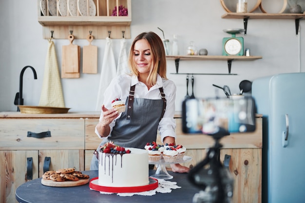 La mujer hace deliciosos dulces y pasteles. Proceso de grabación por teléfono inteligente en trípode.