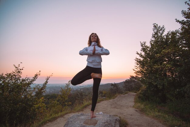 La mujer hace ejercicios de yoga en la cima de la colina al amanecer.