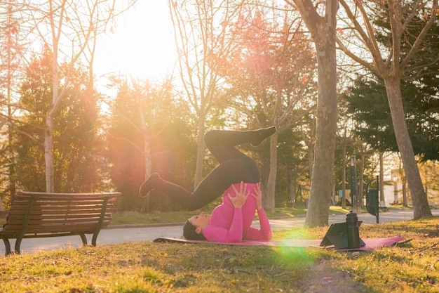 Mujer hace ejercicios de yoga en un parque al atardecer