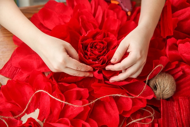 Una mujer hace flores de papel rojas. Solo las manos están en el marco. Vista superior. Foto de alta calidad