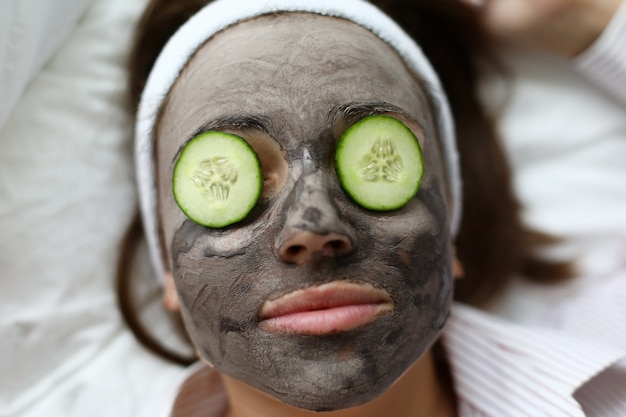 Foto la mujer hace la máscara facial de arcilla gris en casa