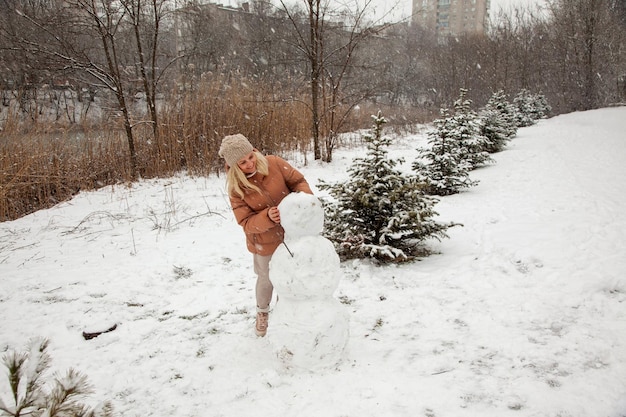 Mujer hace un muñeco de nieve en un parque de la ciudad durante una nevada