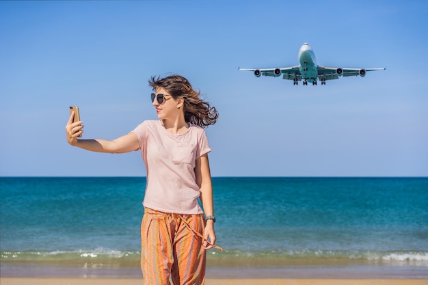 Mujer hace un selfie en la playa viendo los aviones de aterrizaje viajando en un texto de concepto de avión