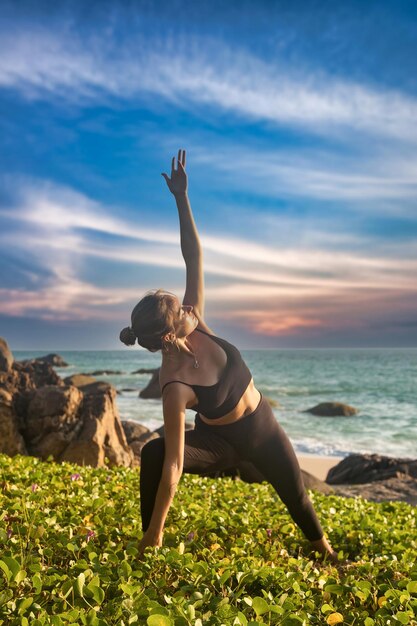 La mujer hace yoga asana para un estilo de vida saludable en el mar tropical o en la playa del océano al aire libre al atardecer