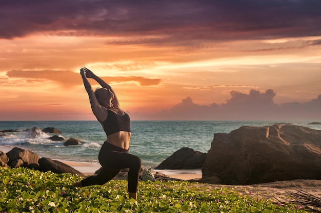 La mujer hace yoga asana para un estilo de vida saludable en el mar tropical o en la playa del océano al aire libre al atardecer