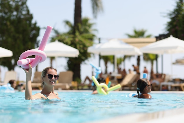 Mujer haciendo aeróbic acuático con fideos en la mano en vacaciones en la piscina en el concepto de resort