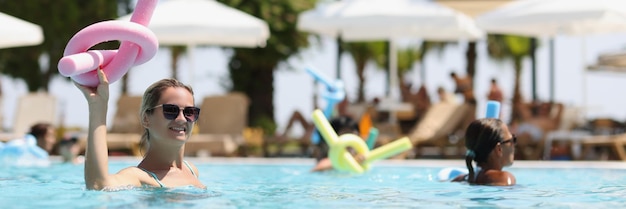 Mujer haciendo aeróbic acuático con fideos en la mano en vacaciones en la piscina en el concepto de resort