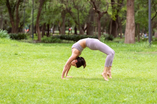 Mujer haciendo asanas de yoga en el parque en el césped con árboles en el fondo