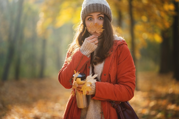 Mujer haciendo cara graciosa con hoja de arce. Soleado bosque de otoño