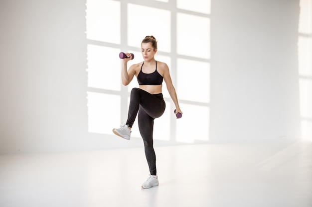 Mujer haciendo cardio con pesas en la sala blanca