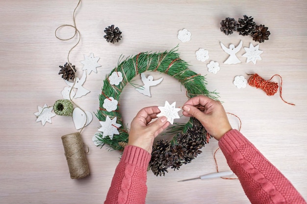 Mujer haciendo una corona de abeto para la víspera de Navidad y decorándola con masa de sal ángeles artesanía festiva