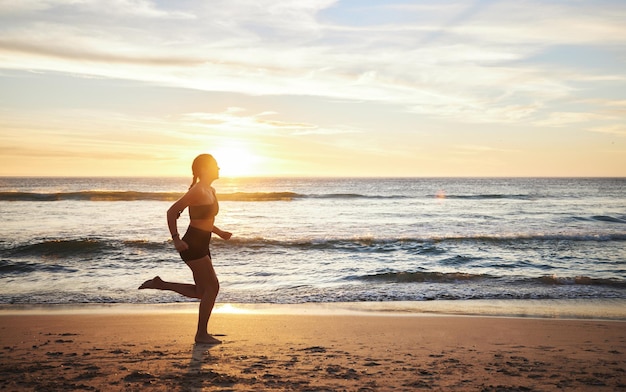 Mujer haciendo ejercicio y corriendo en la puesta de sol en la playa para un entrenamiento cardiovascular saludable o ejercicio al aire libre Corredora haciendo ejercicio al amanecer para correr salud y bienestar junto a la costa del océano