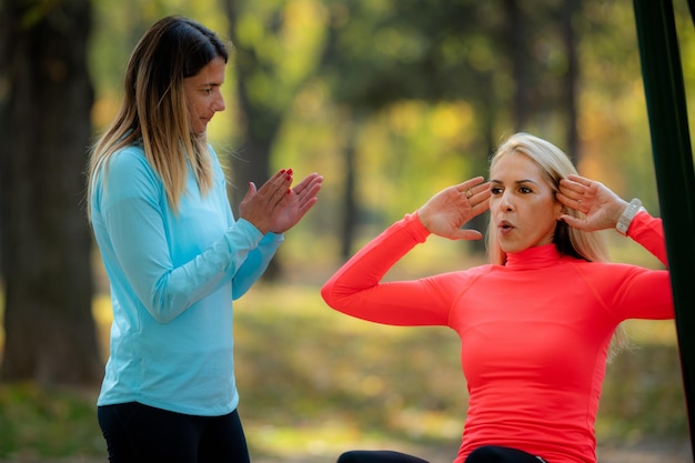 Mujer haciendo ejercicio con entrenador personal en gimnasio público al aire libre en otoño