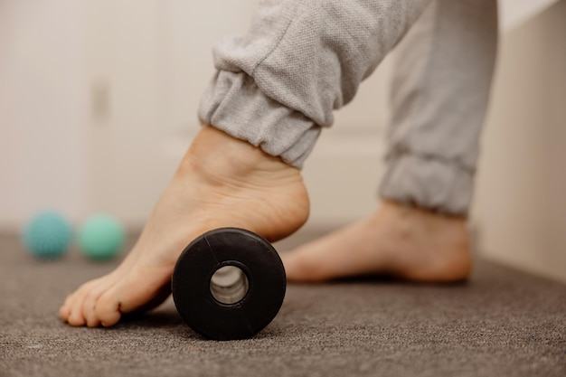 Mujer haciendo ejercicio gimnástico de corrección de pie plano con rodillo de masaje Relajación miofascial de los músculos del pie Hallux valgus Dolor Identificación de pies planos Prácticas de autocuidado en el hogar salud