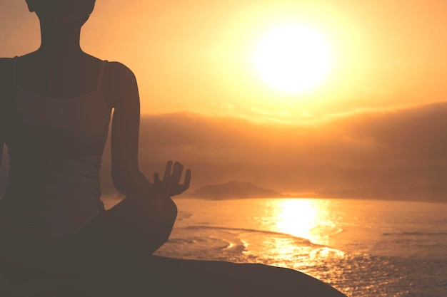 Mujer haciendo ejercicio de yoga en la orilla del mar al atardecer