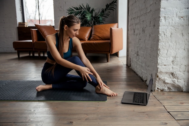 Mujer haciendo ejercicios de fitness en la estera frente a la computadora portátil en casa. Bienestar y concepto de estilo de vida saludable. . Foto de alta calidad. Foto de alta calidad