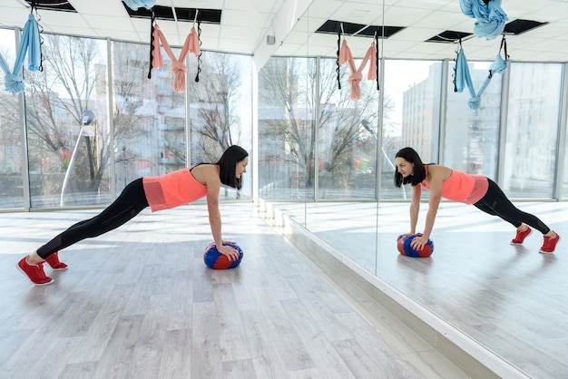 Mujer haciendo ejercicios con pelota ante el espejo en el gimnasio