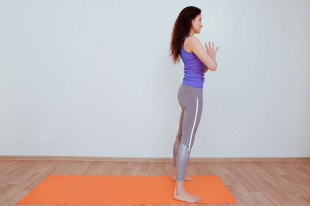 Mujer haciendo ejercicios de yoga en alfombra naranja, estiramiento.