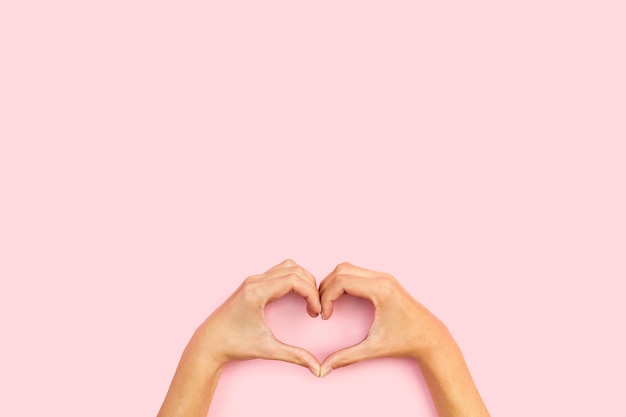 Mujer haciendo forma de corazón con ambas manos sobre un fondo rosa